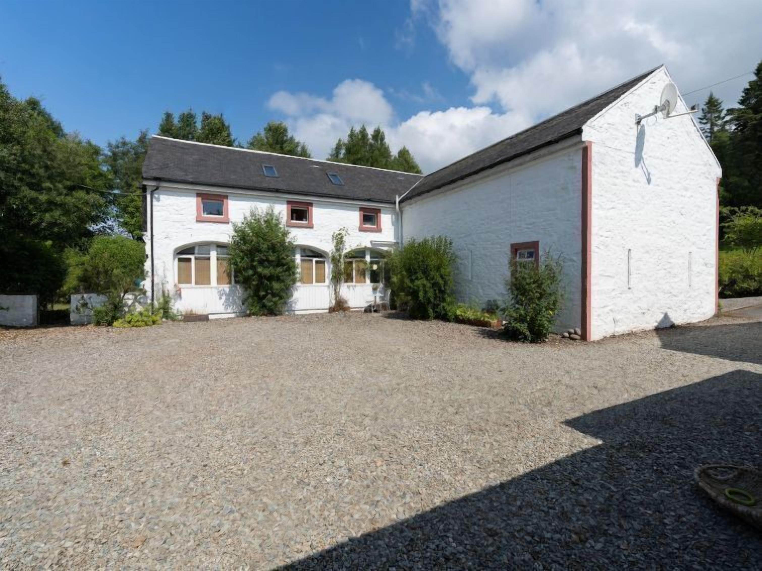 A two-story white building with a gravel driveway and a small garden area.