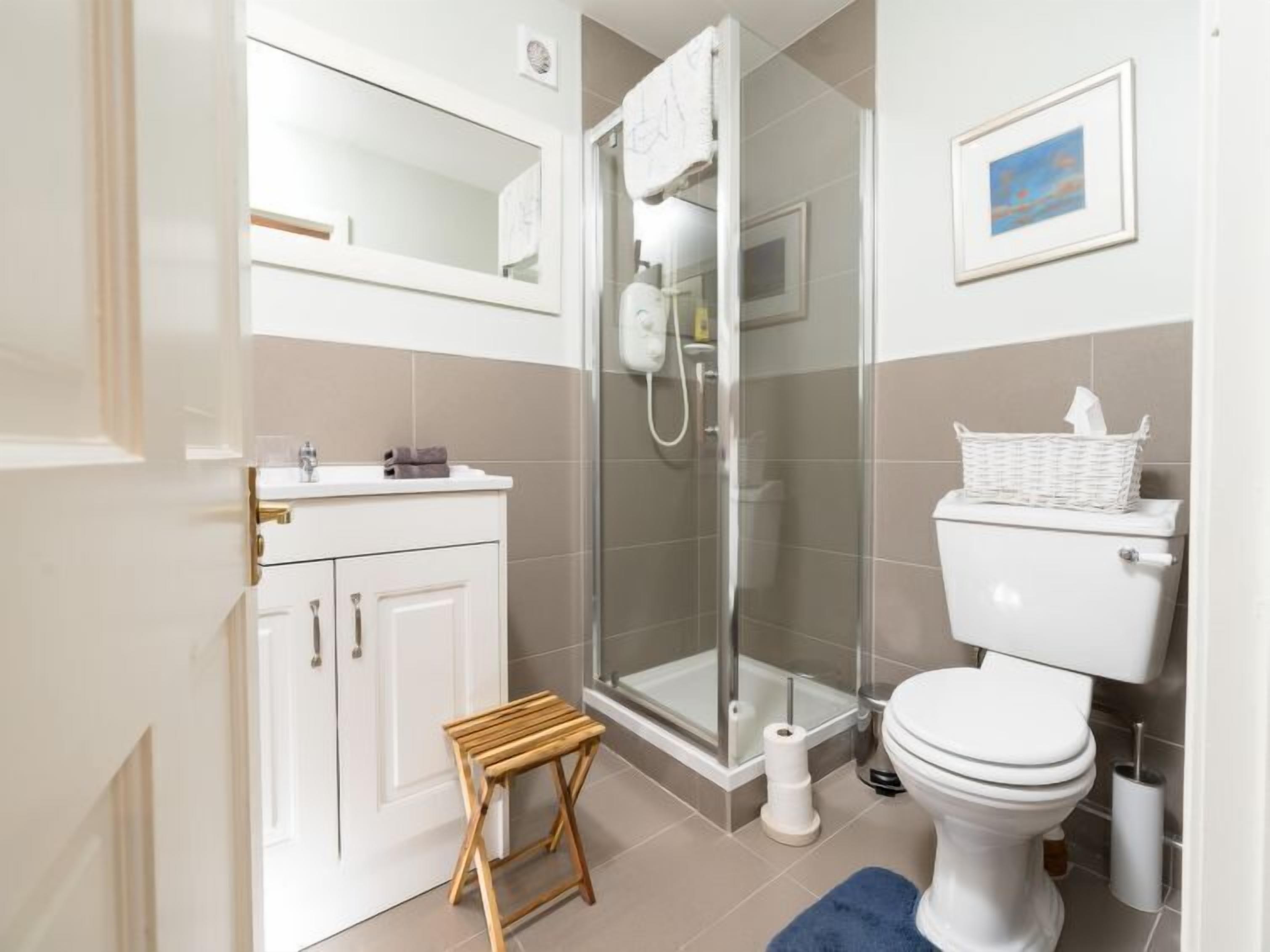 Un baño moderno con cabina de ducha de vidrio, inodoro y un taburete pequeño de madera.