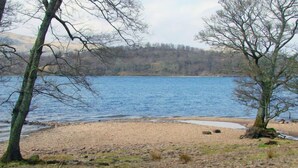 A lakeside view with a sandy beach, trees, and a forested hill in the background. - Lorn Mill by Interhome (Balloch)