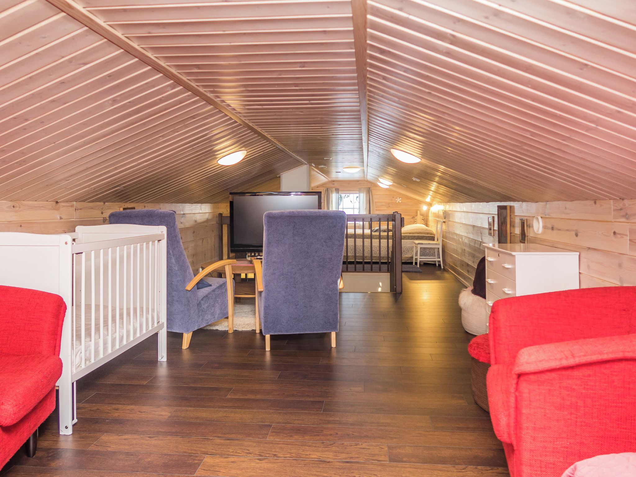 A cozy attic room with a wooden sloped ceiling, a television, a dining table, and two chairs.