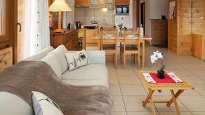 A cozy living room with a sofa, a small table with a potted plant, and a kitchen area with wooden cabinets and a dining table. - Quille du diable 19 by Interhome (Nendaz)