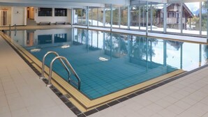 An indoor swimming pool with clear glass walls, a tiled floor, and a view of a mountain landscape. - Quille du diable 19 by Interhome (Nendaz)
