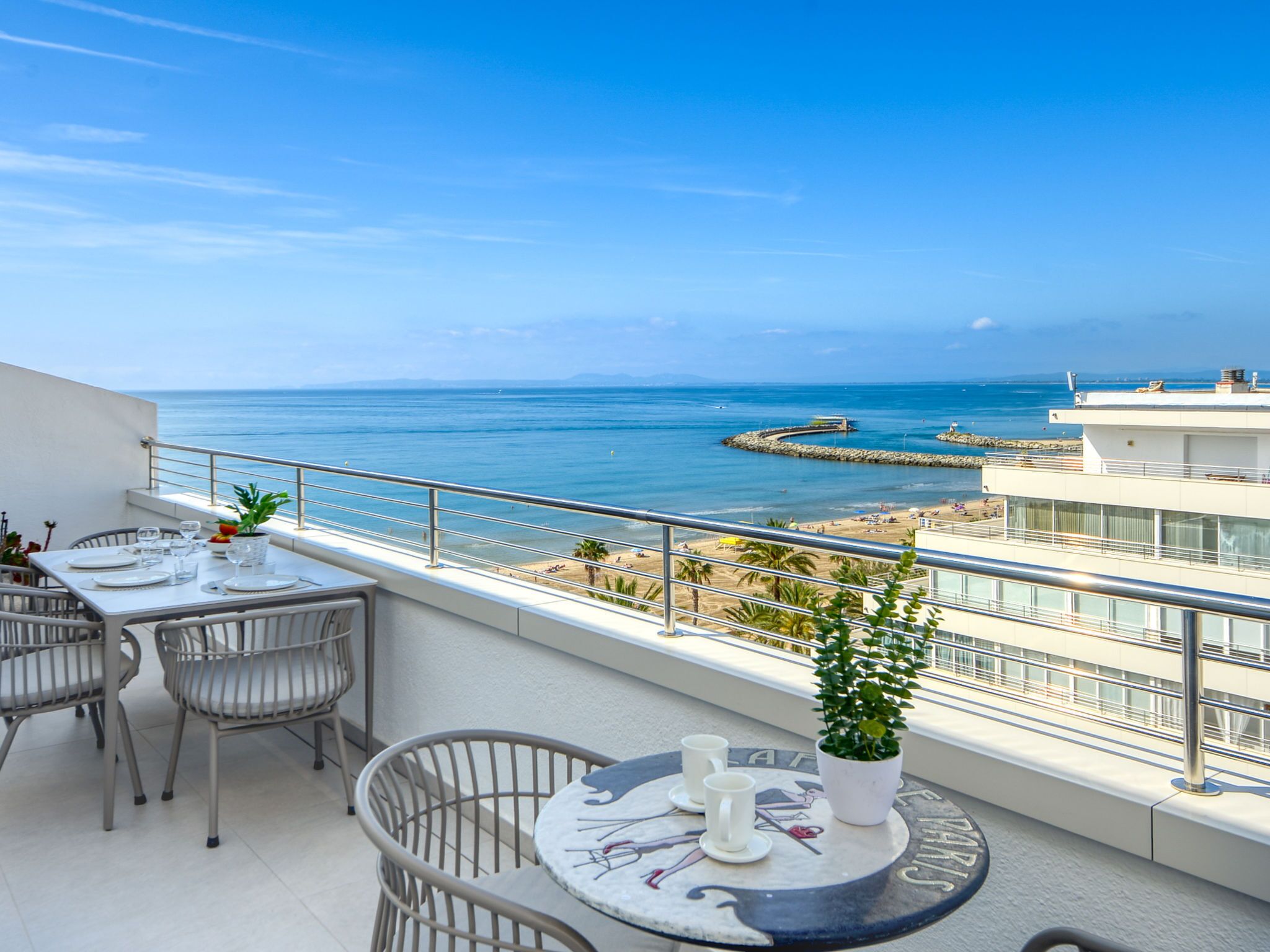 A balcony with a table set for two, overlooking a beach and the sea.