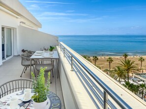 Un balcón con una mesa lista para comer, con vista a una playa de palmeras y al mar.