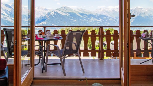 Ein Balkon mit Blick auf schneebedeckte Berge, einem Tisch mit Stühlen und einem Holzzaun.