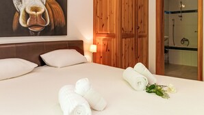 Ein Hotelzimmer mit einem Bett, Kissen, einem Holzschrank, einem Bild von einer Kuh und einem durchgehenden Türspalte sichtbaren Badezimmer.