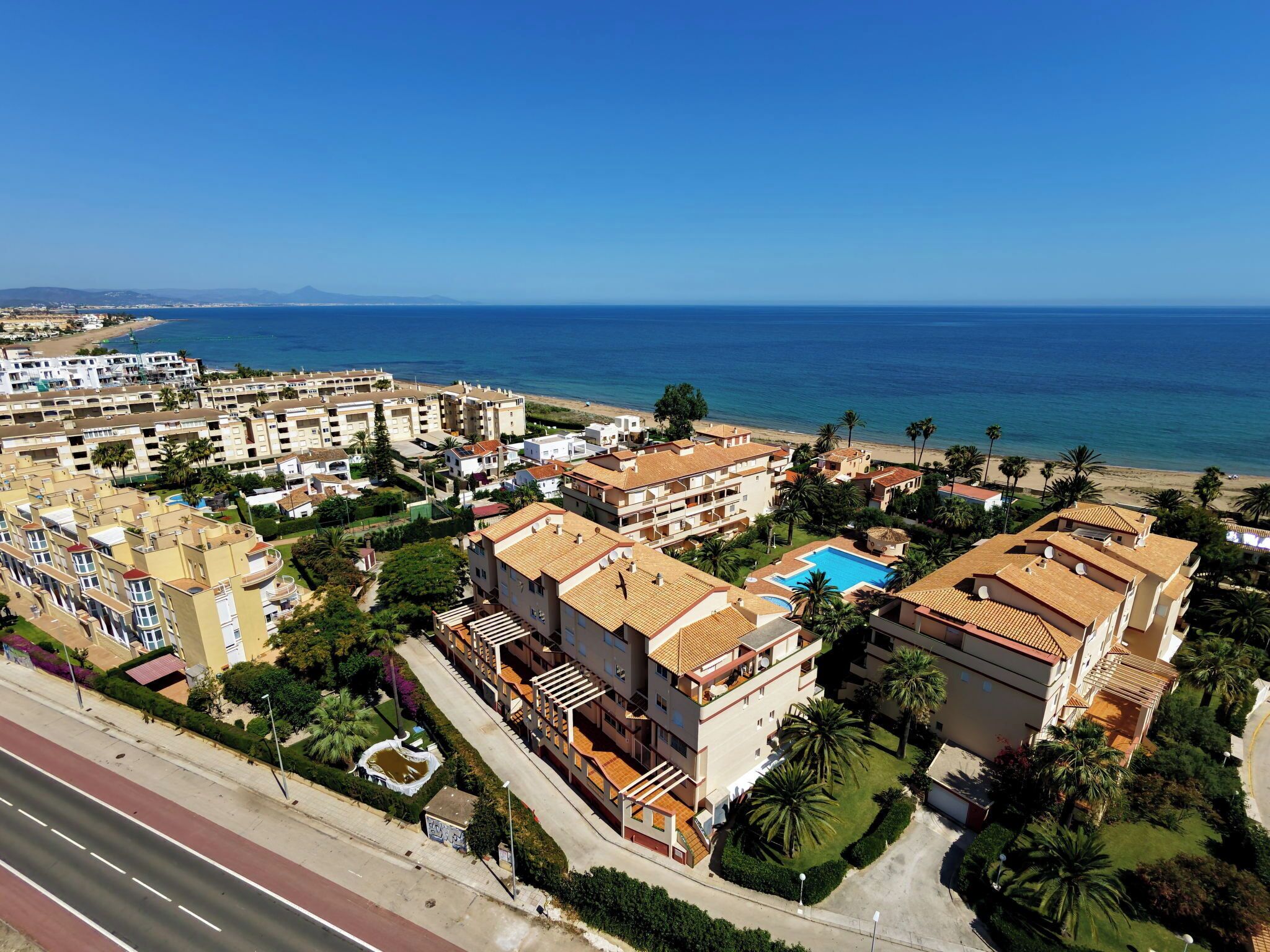 A coastal residential area with multi-story buildings, a swimming pool, and a beach in the background.