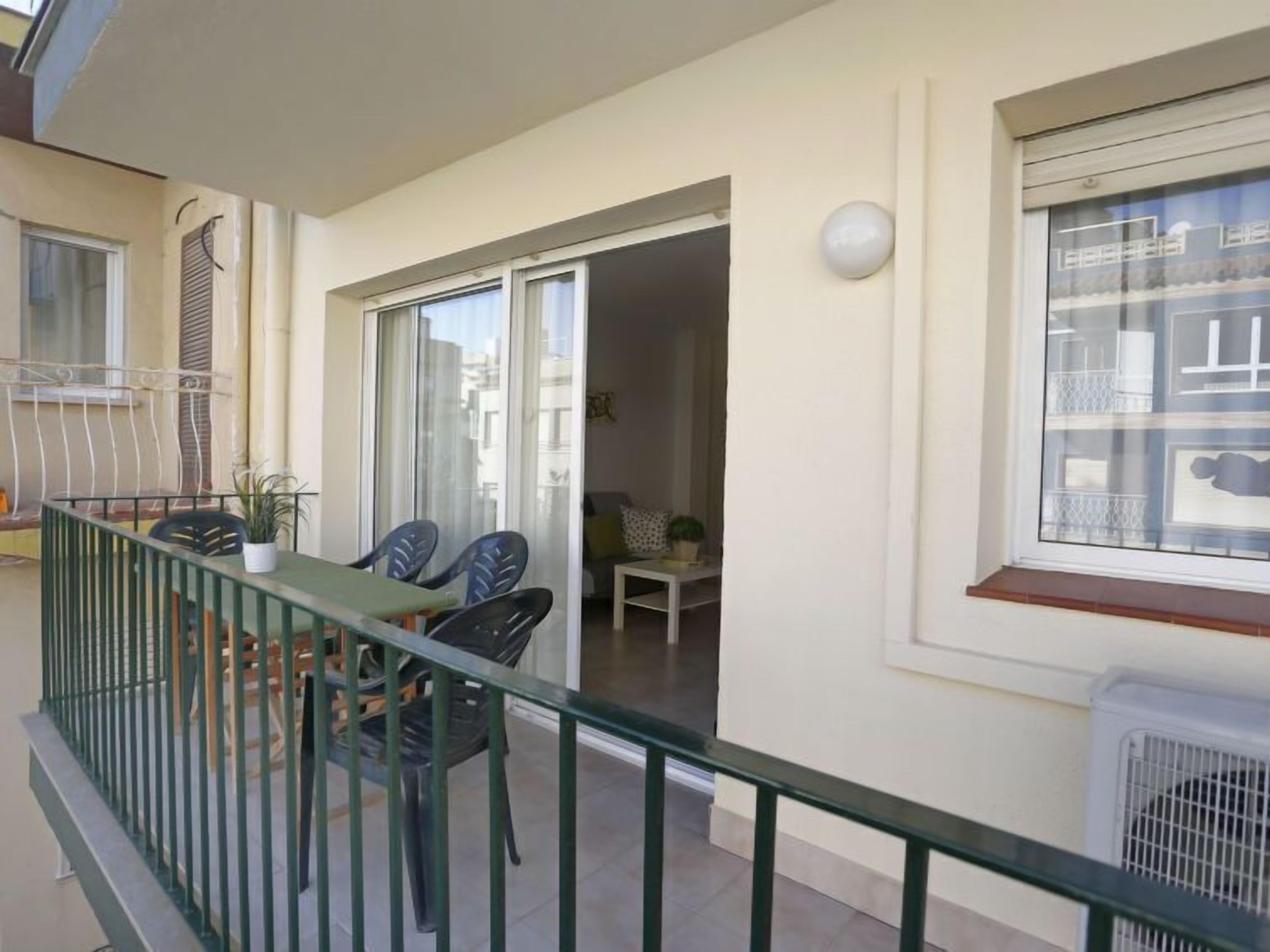 A balcony with a table and chairs, a sliding glass door leading to a living area, and a window with a view of buildings.