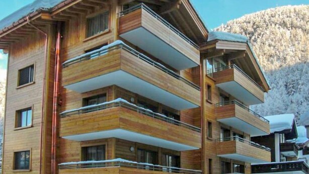 Un immeuble en bois à plusieurs étages, doté de balcons, qui se dresse sur un fond de paysage montagneux.