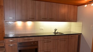 A kitchen with wooden cabinets, a stainless steel oven, and a black countertop.