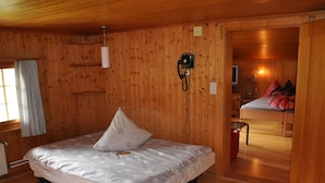 A wooden-paneled room with a bed, a telephone, and a visible doorway leading to another room.