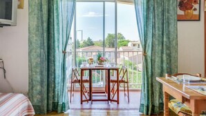 Una habitación con una mesa de comedor y sillas, una cama con colcha a rayas y una ventana con cortinas.