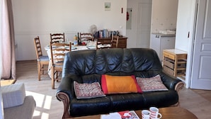 Ein Wohnzimmer mit schwarzem Ledersofa, einem Esstisch mit Stühlen, einer Küchenzeile und einer Tür.