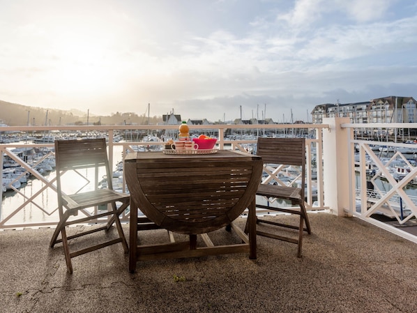 Una mesa de madera con sillas en un balcón con vistas a un puerto deportivo lleno de barcos.