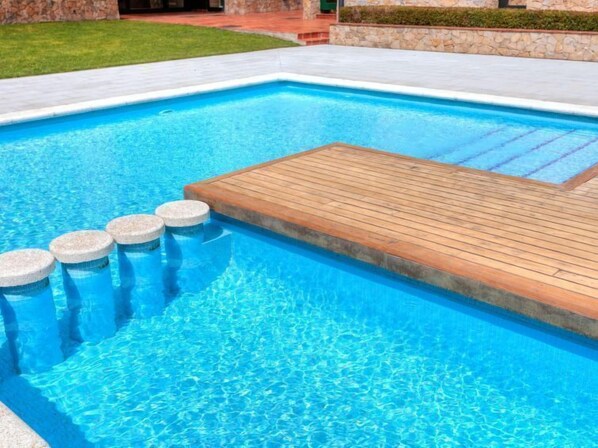 A rectangular swimming pool with a wooden deck and stone steps leading into the water.