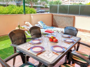 A patio with a table set for four, surrounded by chairs, a small fruit bowl, and a bottle.