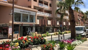 Un edificio de varios pisos con balcones, una tienda con un letrero que dice "boudoir du regard", y una variedad de flores coloridas al frente.