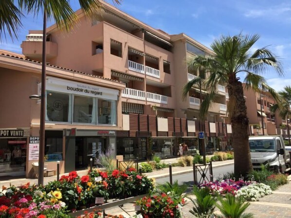 A multi-story building with balconies, a storefront with a sign reading "boudoir du regard," and a variety of colorful flowers in the foreground. - Apartment Régina by Interhome (Sainte Maxime)