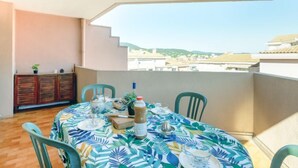 Un balcón con mesa lista para comer, sillas, una planta en maceta y vistas a edificios a lo lejos.