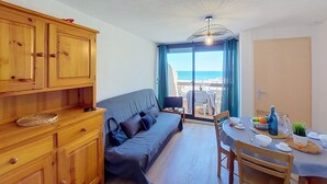 Ett rum med en soffa, träskåp, ett matbord med stolar och utsikt över stranden.