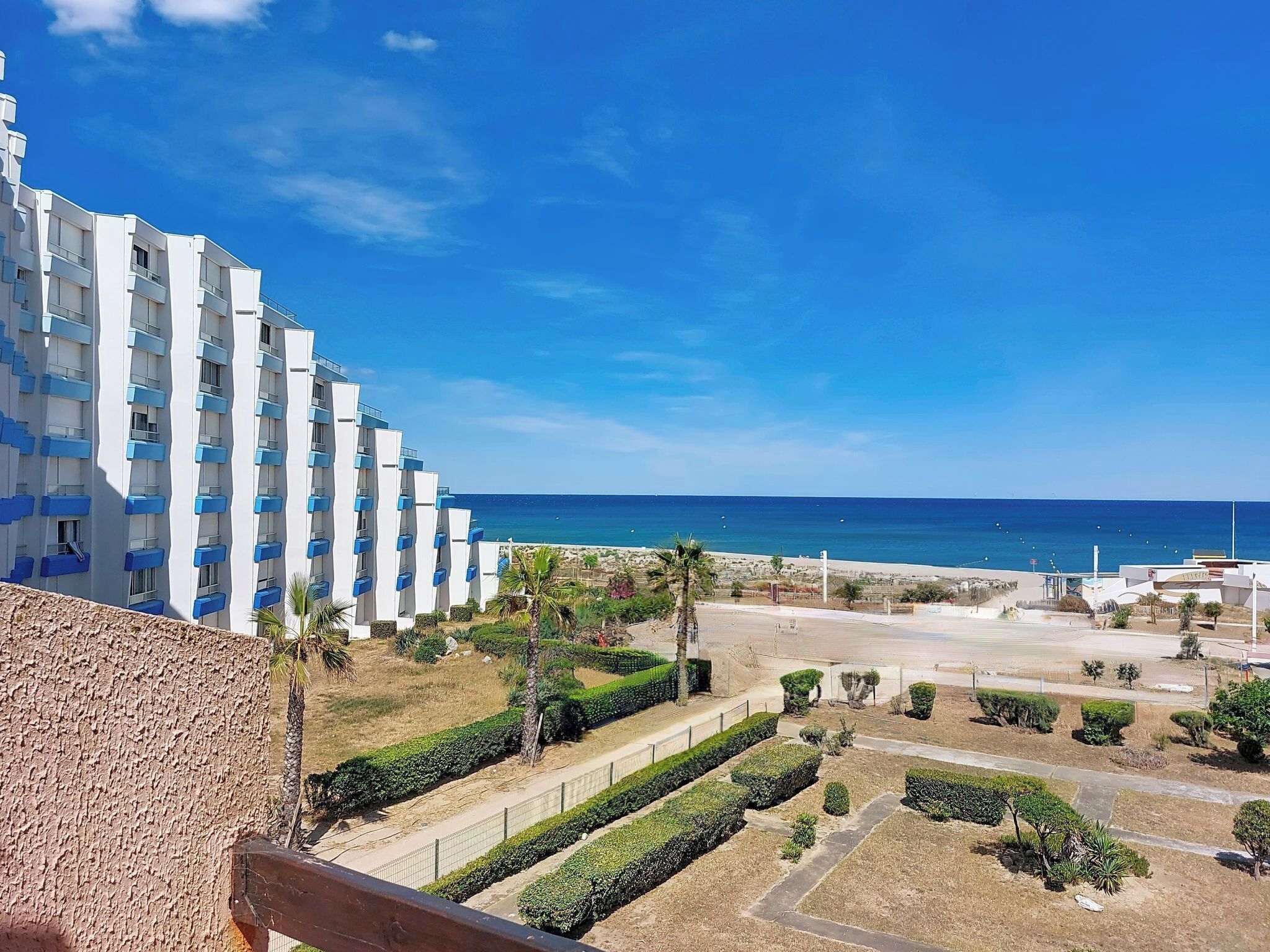 Ein modernes Hotel mit Blick auf das Meer, einem angelegten Garten und blauem Himmel.