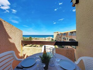 Un balcon avec une table dressée pour deux personnes, donnant sur une plage et des bâtiments.