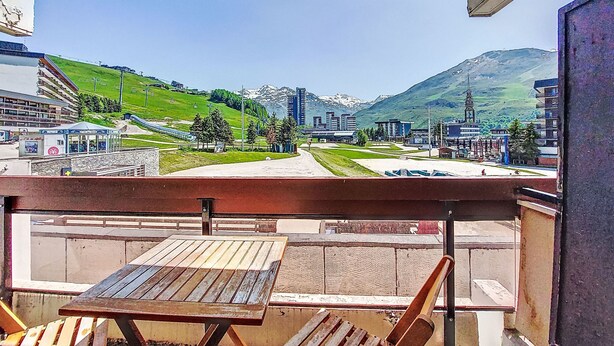A balcony with a wooden table and chairs, overlooking a cityscape with buildings and a mountain in the background. - Chavière 120 by Interhome (Les Menuires)