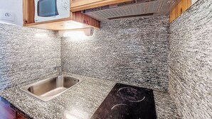 A kitchen with granite countertops, a stainless steel sink, wooden cabinets, and a microwave. - Chavière 120 by Interhome (Les Menuires)