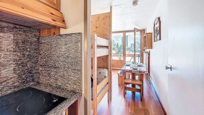 A narrow hallway with wooden cabinets, a black stove, and a dining area with a table and chairs. - Chavière 120 by Interhome (Les Menuires)
