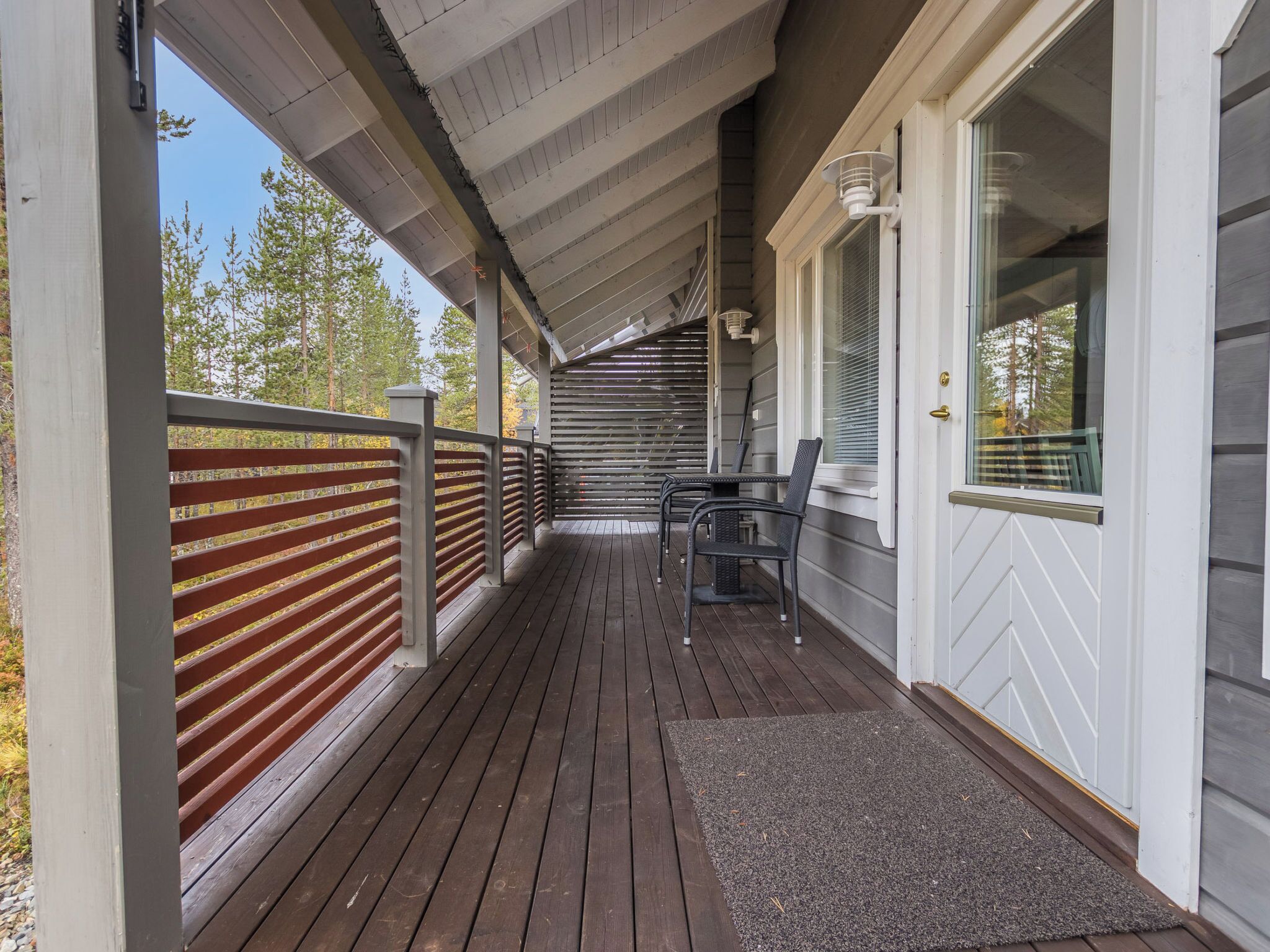 A covered porch with a wooden deck, a metal railing, and a door with a window.