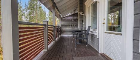 A covered porch with a wooden deck, a metal railing, and a door with a window.