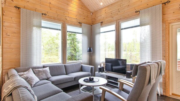A modern log cabin interior with a grey sectional sofa, a small round table, a TV, and a chair with a towel.