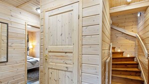 A wooden interior with a central door, a staircase, and a bed with a headboard.