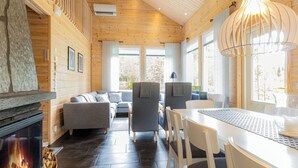 A cozy cabin interior with a fireplace, wooden walls, and a dining area.