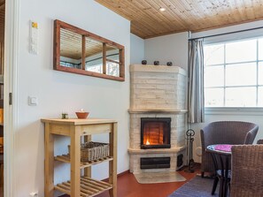 Une pièce chaleureuse avec une cheminée, une étagère en bois, des meubles en osier et une fenêtre avec des rideaux.