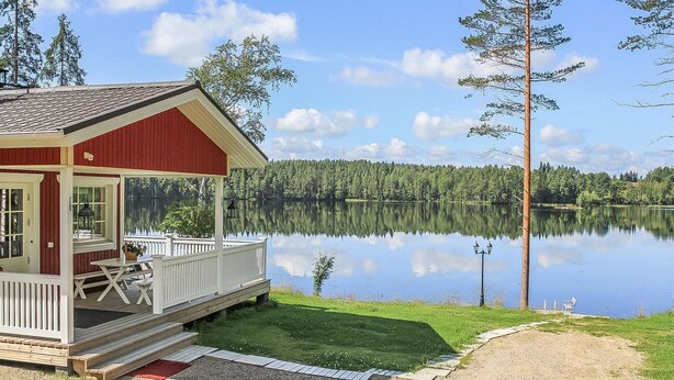 A lakeside cabin with a covered porch, a small deck, and a view of a calm lake surrounded by trees. - Villa akuliina by Interhome (Multia)