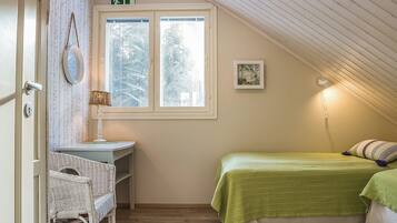 Ett rum med ett sluttande tak, ett fönster med frostat glas, ett skrivbord med en stol, en säng med grönt sänglinne och en tavla som hänger på väggen.