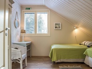 A room with a sloped ceiling, a window with frosted glass, a desk with a chair, a bed with green bedding, and a wall-mounted picture. - Villa akuliina by Interhome (Multia)