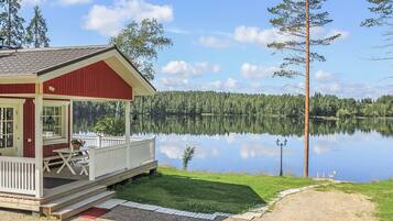 En stuga med en veranda, en brygga och utsikt över en lugn sjö omgiven av träd.