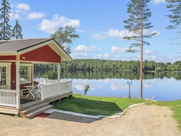 A cabin with a deck, a dock, and a view of a calm lake surrounded by trees.