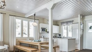 A modern kitchen with white cabinetry, a wooden dining table, and a built-in island. - Villa akuliina by Interhome (Multia)