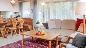 A cozy living room with a wooden ceiling, a sofa, a coffee table with fruit, and a dining area with chairs and a table. - Zur Linde Apt.W by Interhome (Wengen)