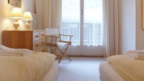 A hotel room with two beds, a small desk, a chair, and a window with curtains. - Zur Linde Apt.W by Interhome (Wengen)