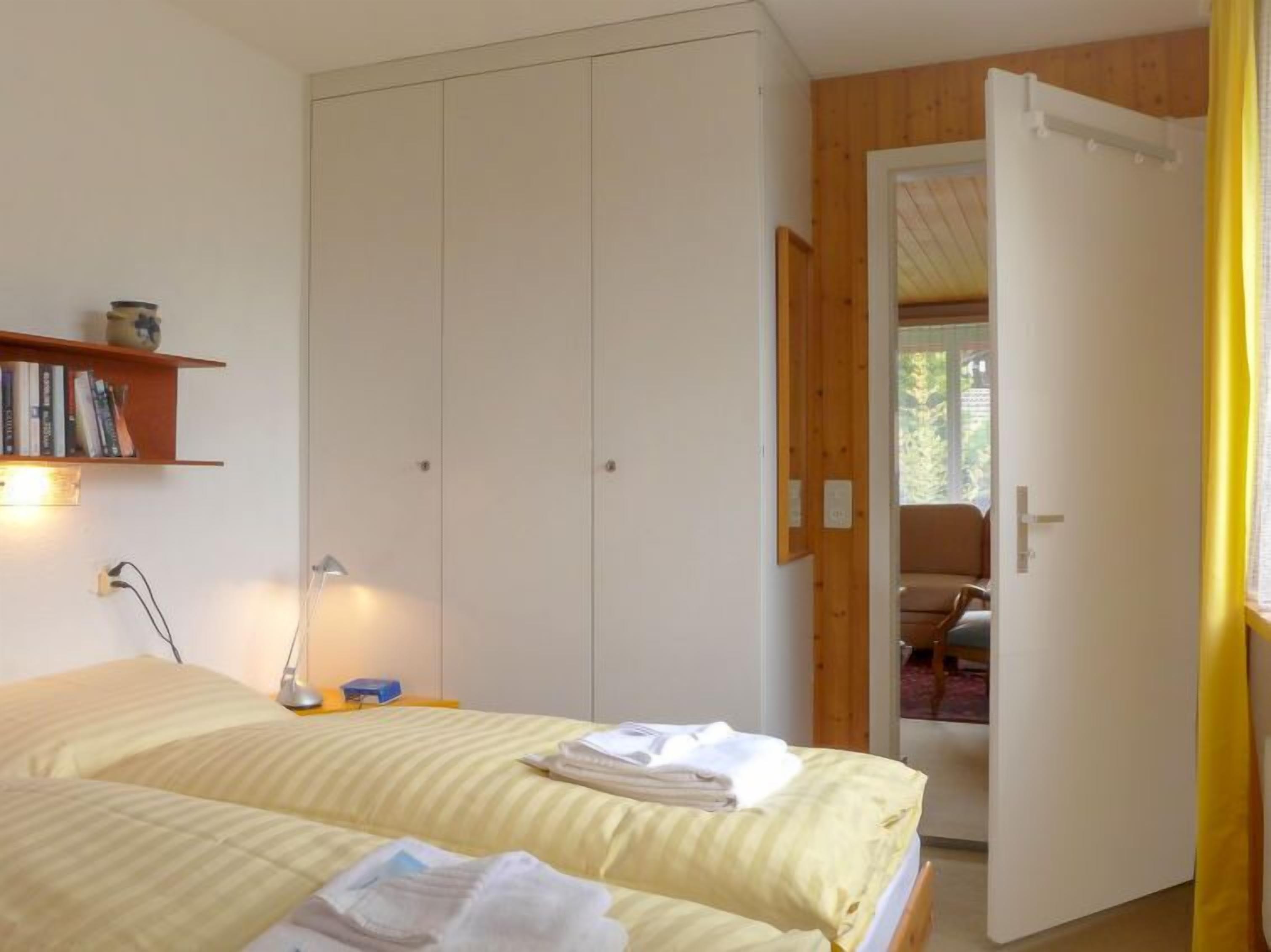 Ein Schlafzimmer mit zwei Betten, einem Nachttisch mit Lampe, einem Bücherregal und einem Kleiderschrank.