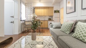 A modern kitchen with wooden cabinets, a dining area with a table and chairs, and a living room with a sofa and cushions.