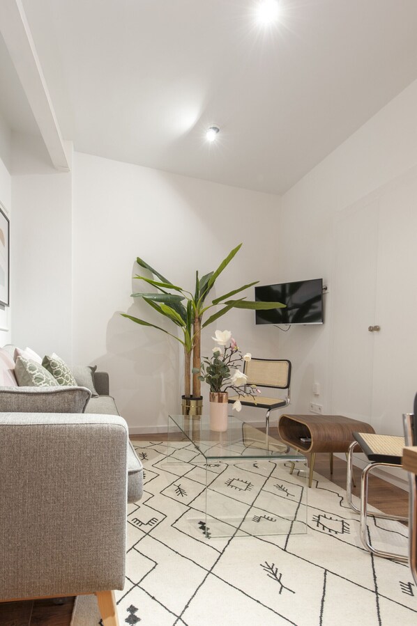 A modern living room with a sofa, a coffee table, a TV mounted on the wall, and a large plant.