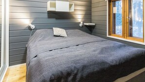 Makuuhuone, jossa on sänky, yöpöytälamput, yöpöytä, ikkuna ja seinälle kiinnitetty hylly.