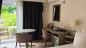 A hotel room with a bed, a desk, a chair, a small table, a coffee maker, a lamp, and a window with curtains.