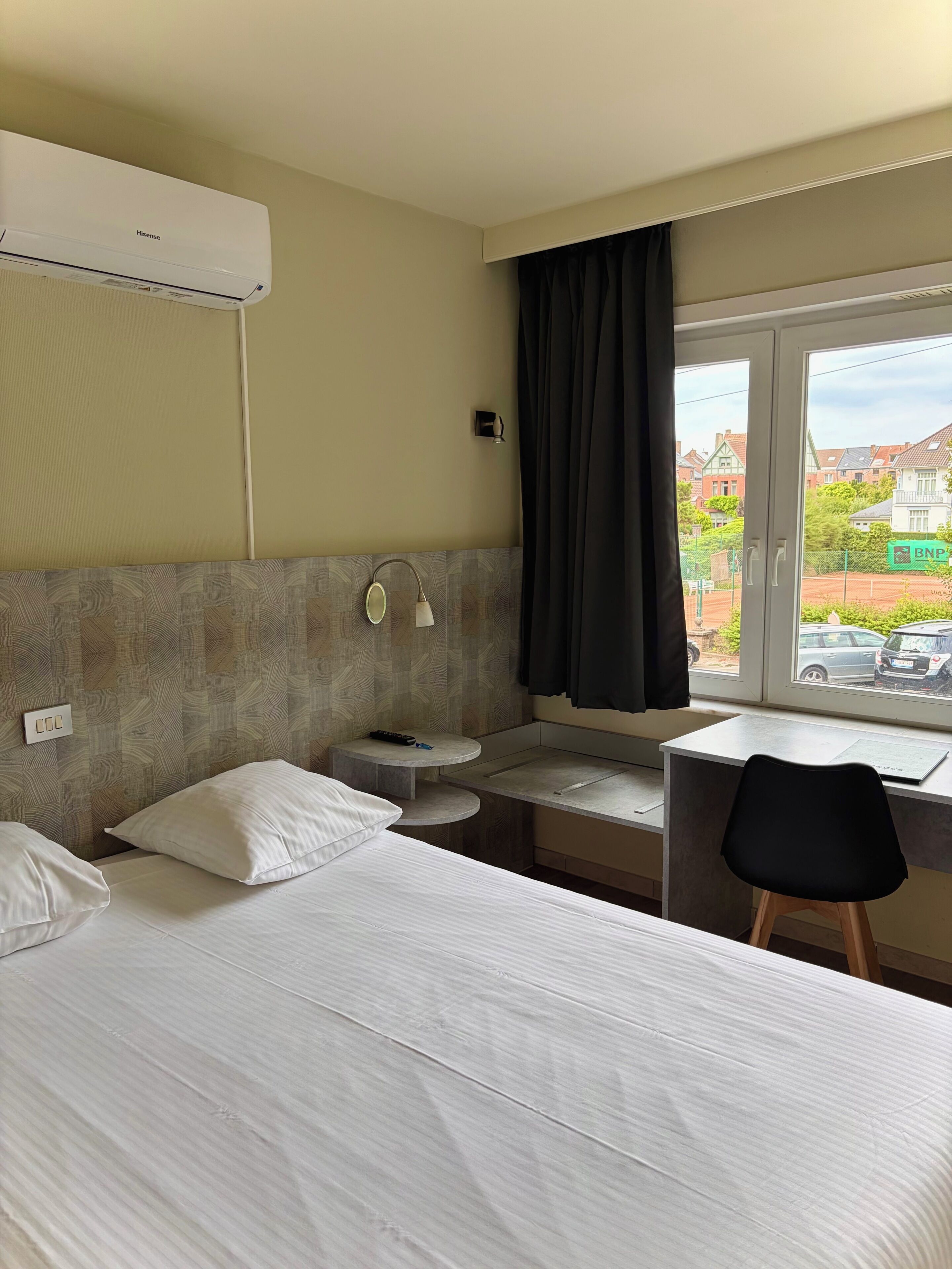 Una camera d'albergo con un letto, una scrivania, un tavolino, una finestra con tende e un condizionatore.