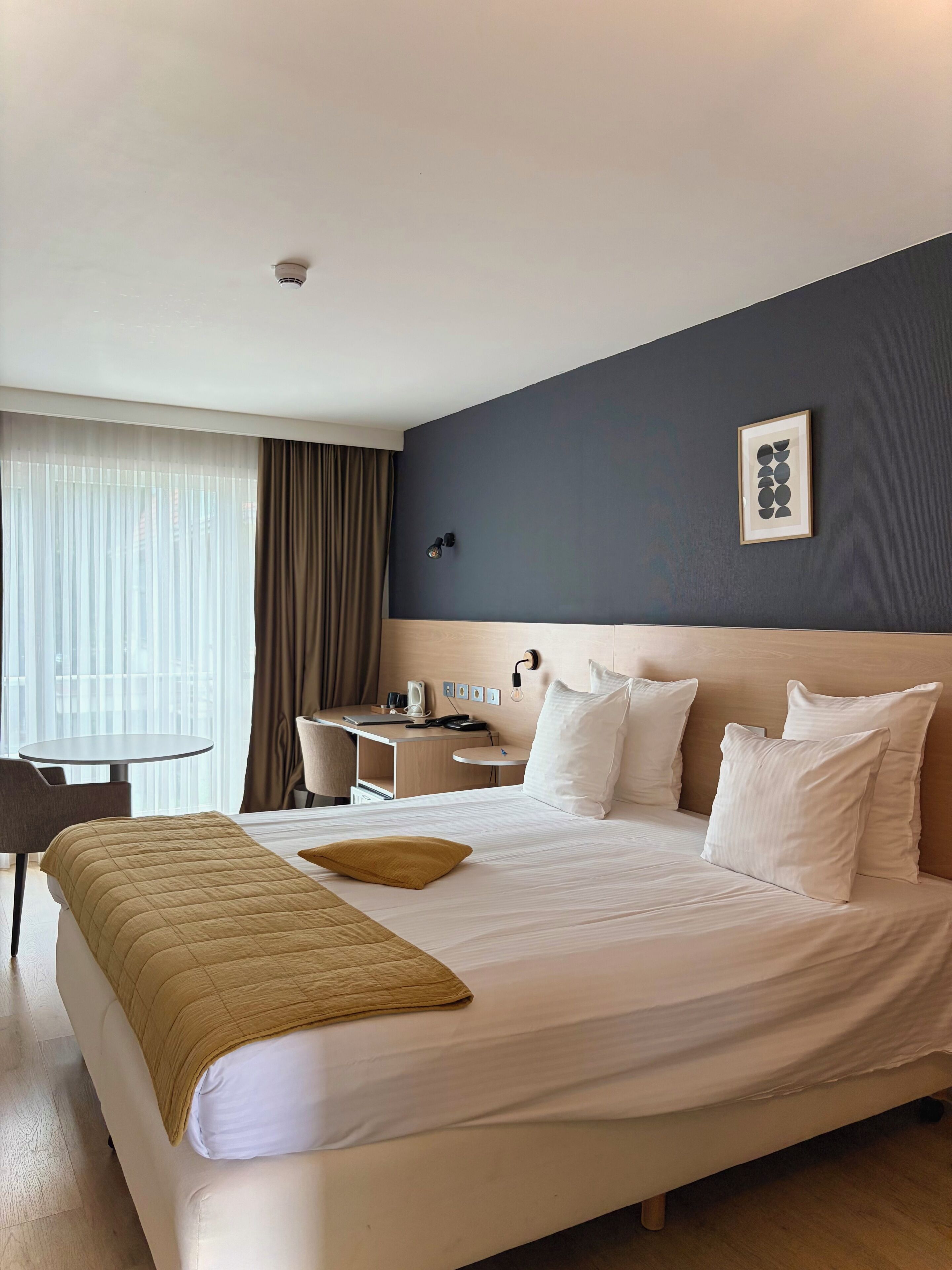 A hotel room with a large bed, a desk, a chair, and a window with curtains.